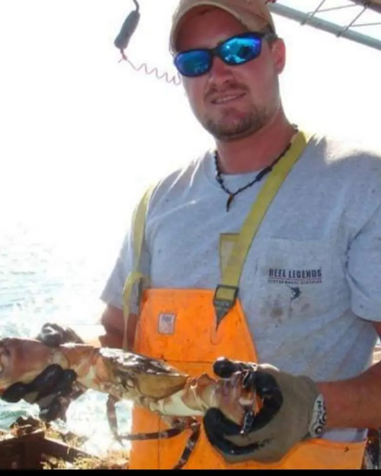A live stone crab held up on the boat by a crewman in orange bibs